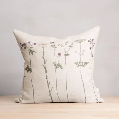 Beige kudde i 100 % linne med blommor som mönster, tillverkad av NORDRÅ Sweden som säljer presenter och inredning.