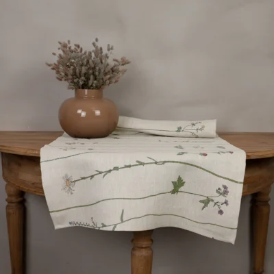 Beige bordslöpare i 100 % linne med blommor som mönster, tillverkad av NORDRÅ Sweden som säljer presenter och inredning.